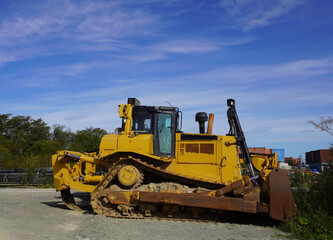 A yellow excavator on the road. A yellow crawler excavator is parked on the side of the road against a blue sky background.