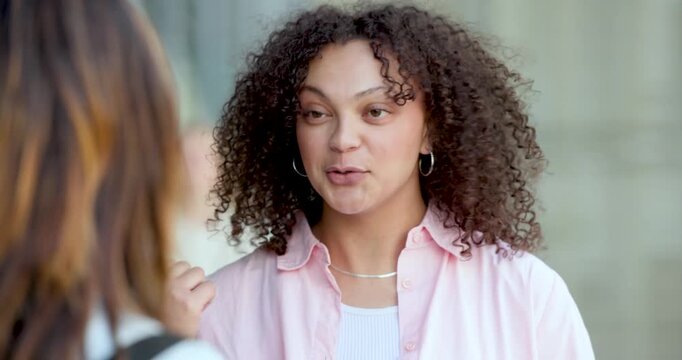 Two women talking on city sidewalk, African American woman smiling then making point in pink shirt
