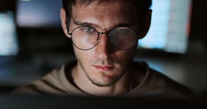 White Caucasian male software developer work late night, program coding in home office. Computer engineering job, data scientist, cybersecurity, information technology. Close-up eyeglasses, handheld