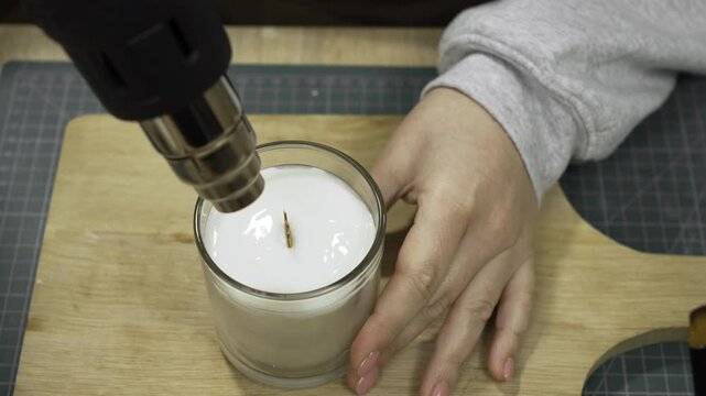 female hands melting wax in homemade candle with professional construction dryer indoors