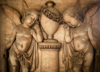 Couple of young angels, crying for the loss. Sculpture on ancient tombstone in an old Italian cemetery