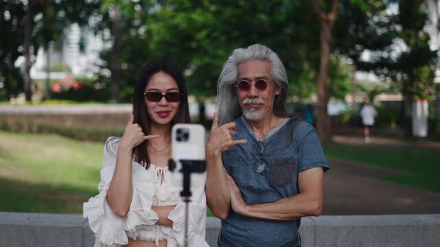 Asian senior man and young woman have fun making a tik tok and recording it with a smartphone in a city park