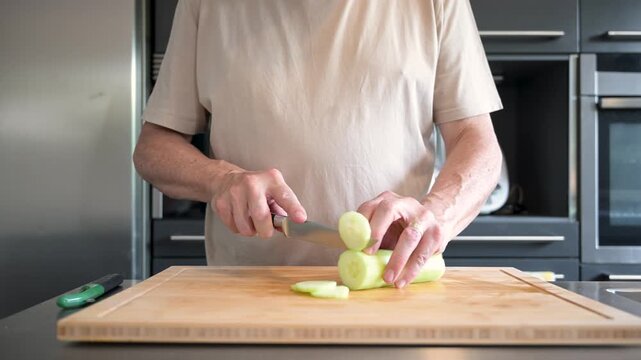 Senior man slicing a fresh cucumber in a modern kitchen