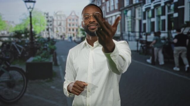 Man showing middle finger to camera on a cobbled city street lined with bicycles and canal houses wearing white shirt and glasses; defiance.