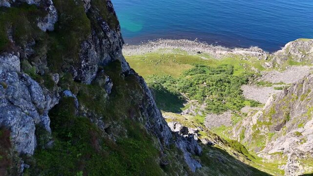 Forward turn drone flight above, top view of cliffs ofLaupen mountain peak on Vesteralen, Vester&aring;len islands. Next to rocks revealing rocky beach, blue ocean. Outdoor travel destination. Impressive cl