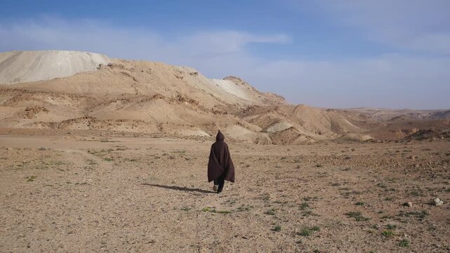 Person wearing traditional Tunisian desert attire walking across a rocky arid landscape in southern Tunisia, symbolizing heritage, nomadic culture, and timeless connection to the land