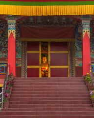 Peaking behind the door of magical interior of a Tibetan temple with a golden statue of a seated Buddha in Tibetan monastery near Pokhara, Nepal.