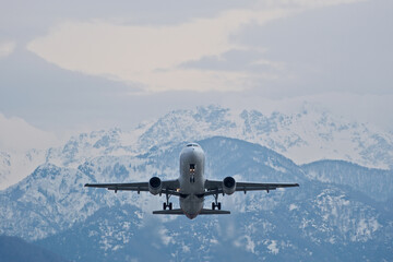 White Airplane Taking Off Against Snowy Mountains in Cloudy Weather