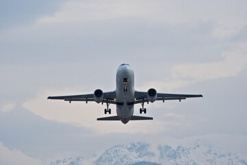 White Airplane Taking Off Against Snowy Mountains in Cloudy Weather