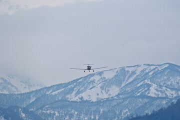 Light single-engine airplane climbing over snow-capped mountains in cloudy weather