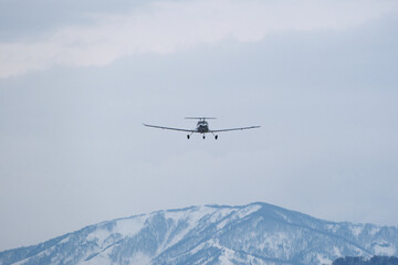 Light single-engine airplane climbing over snow-capped mountains in cloudy weather