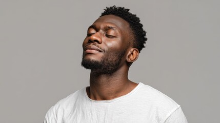 Obraz premium An African man in a white t shirt stands with eyes closed against a grey background exuding a sense of calm and harmony perfect for creative advertising