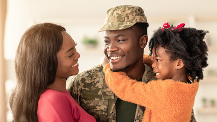 A soldier returns home to embrace his family. He smiles at his partner and daughter, who are joyful...