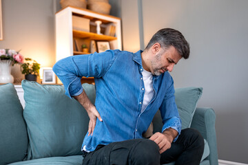 Pain in the back. Lower back pain, People with spine-muscles problem, Healthcare And Medicine concept. Man sitting on the sofa and holding painful lower back with hand. Suffering from sciatica strain.