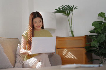 asian woman sitting on sofa using laptop for surfing an internet