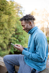 Obraz premium African American man using smartphone in nature, connecting with technology outdoors
