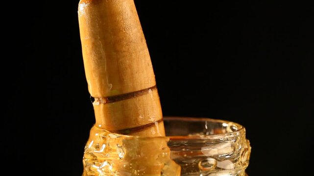 Drops of thick golden honey flowing down on a black background. Close up of sweet nectar or molasses being spilled. Liquid honey pours and drips. Sugar syrup is pouring. Healthy and curative dessert