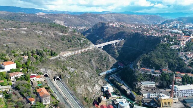 Aerial view of Rijeka, Croatia, showcasing its dramatic river canyon, historic Trsat Castle, and modern infrastructure under a partly cloudy sky.