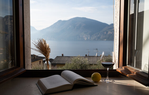 Lake Garda view through window with wine glass and lemons on table. Italian vacation mood, slow living and romantic lifestyle concept.