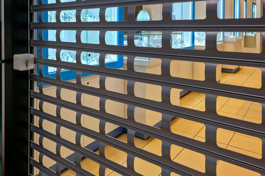 Jewelry store secured with metal roller shutter revealing illuminated luxury display cases inside