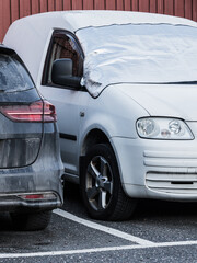 Cars parked in a lot in Sweden with one vehicle covered on a winter day