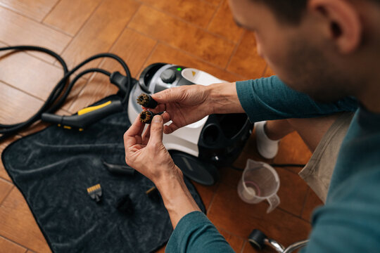 View from shoulder shot of man holding two steam-cleaner brushes side by side, one worn with matted bristles and one new with stiff bristles. Concept of maintenance, replacement.