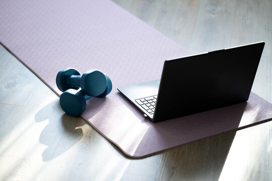 Laptop, dumbbells and resistance band on yoga mat at home. Online fitness training, home workout equipment, modern healthy lifestyle and digital fitness concept.

