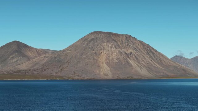 Aerial view reveals a gentle pan over Rumilet Bay and barren mountains. The shot holds steady waterline in Chukotka in early autumn. Bright clear sky with minimal clouds and long horizon