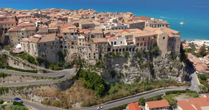 Aerial panorama of the town of Tropea, Calabria, Italy. The houses and buildings of the historic center are perched on the edge of high sandstone cliffs, overlooking the turquoise Mediterranean sea.