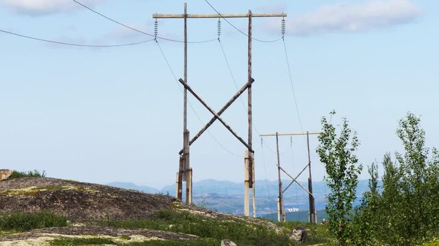 Old wooden poles of a power line in the rocky mountain tundra on a bright sunny summer day.