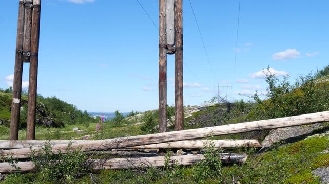 Old wooden poles of a power line in the rocky mountain tundra on a bright sunny summer day.