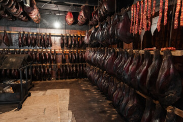 Dark interior scene of a meat-curing cellar with rows of hams