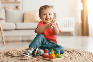 Adorable toddler boy playing with educational wooden toy at home, clapping hands and smiling at...