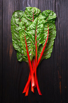 Fresh chard leaves with red stalks laid flat on rustic wood. Healthy organic greens concept
