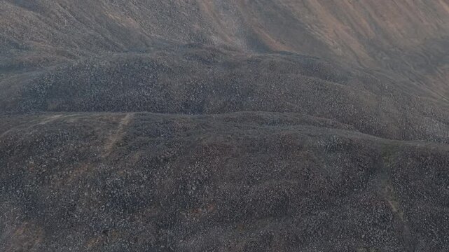 Aerial drone footage drifts over tundra hills near Bering Strait and Provideniya, Chukotka. Subtle lateral movement shows rocky slopes. Late summer evening calm under clear sky