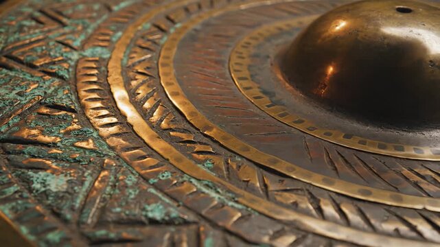 Close up of an ancient bronze artifact with intricate geometric patterns and weathered patina showcasing detailed craftsmanship and historical texture with warm lighting illuminating the metallic