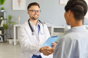 Fototapeta premium A doctor with a clipboard and a stethoscope greets a patient with a smile and a handshake to build trust during the consultation. Doctor and patient begin a respectful talk.