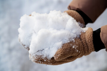 Person holding a pile of fluffy snowflakes in brown fleece gloves. Detail of fresh precipitation after a heavy snowfall or blizzard. Photo © slexp880
