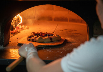 Obraz premium Baker placing a rustic fruit galette into a hot wood-fired brick oven with a wooden peel