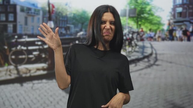 Woman pinches nose and waves hand on a cobblestone street beside a canal with bicycles nearby; disgust avoidance repulsion.