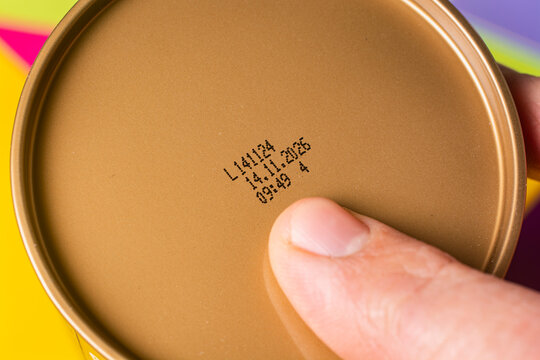 A man checks the production date and expiration date of a product on a can with his index finger.
