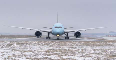 Front view of a commercial passenger airplane taxiing on a snowy airport runway in winter