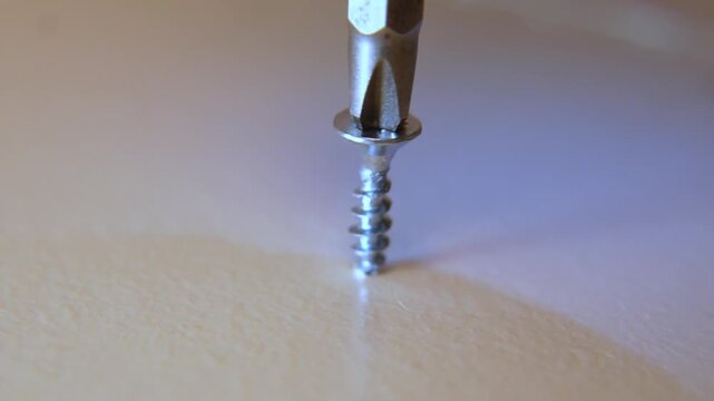 macro close up of steel screw being driven into wooden furniture surface with phillips bit in slow motion showing craftsmanship during home repair or construction work