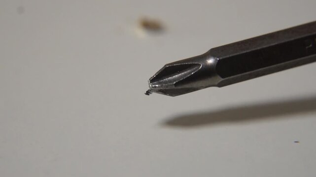 macro close up of metal crosshead phillips screwdriver bit spinning in slow motion against blurred neutral background showing industrial precision and metallic texture of rotating tool