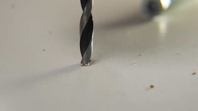 macro close up of sharp spiral metal drill bit spinning in slow motion and starting to penetrate white surface with high precision during industrial work or home renovation