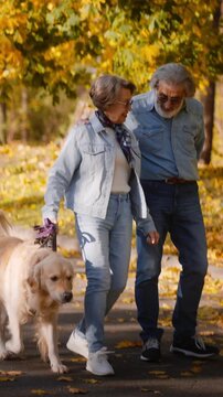 Overjoyed mature couple taking pet for walk in autumn park
