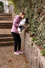 Girl cuddling her puppy while standing near a stone wall