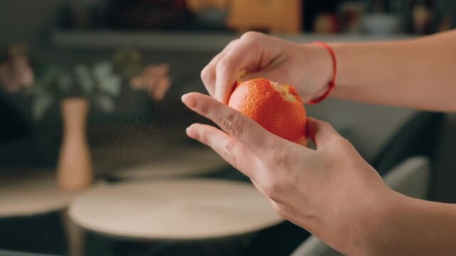 Slow-motion of female hands peeling ripe tangerine, juice droplets exploding in air, perfect for culinary ads, social media content, and lifestyle videos.