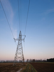 Low angle view of a high voltage transmission tower and overhead power lines over rural farmland under a clear sky, illustrating electricity grid and energy infrastructure.
