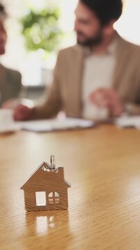 Close-up angle of house keychain on table, blurred couple in background, video concept of home buying